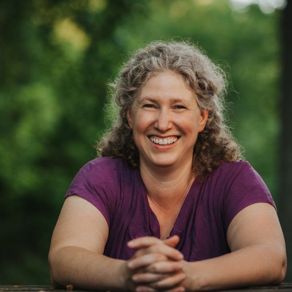 Rachel Becker Klein smiles for a headshot while she leans with her hands intertwined in front of her. 